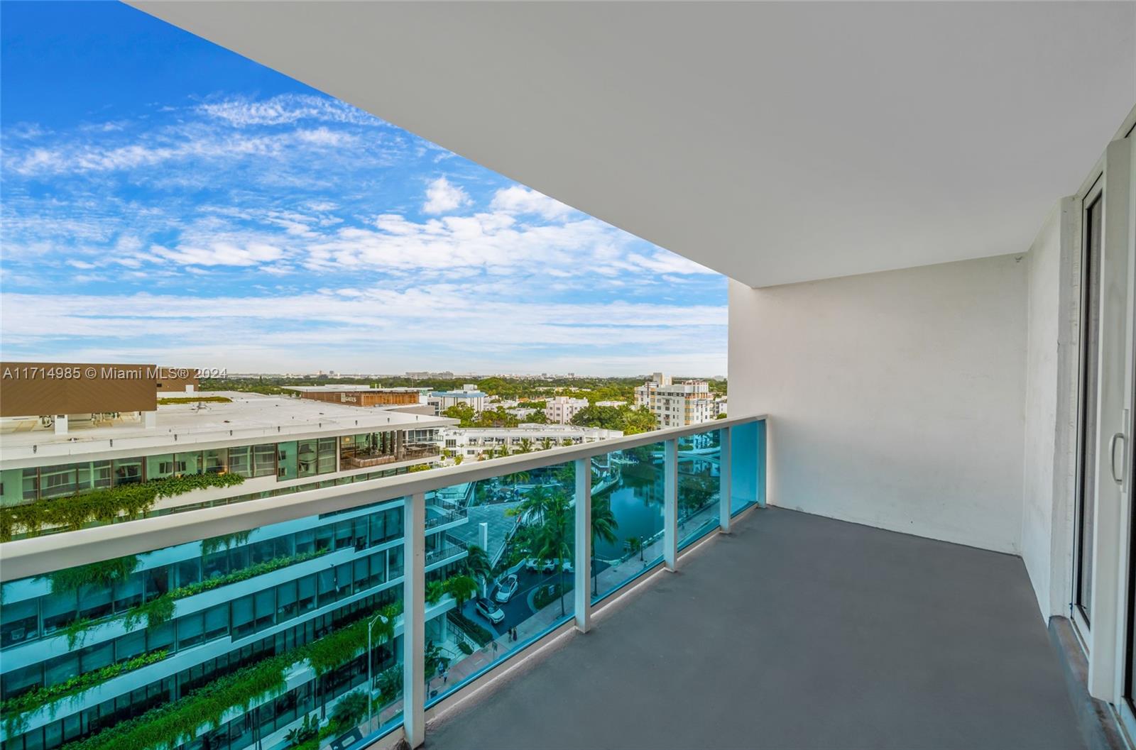 A balcony with a glass railing overlooks a city street and a canal — 2301 Collins Ave # 1030, Miami Beach FL 33139, MIAMI BEACH, FL