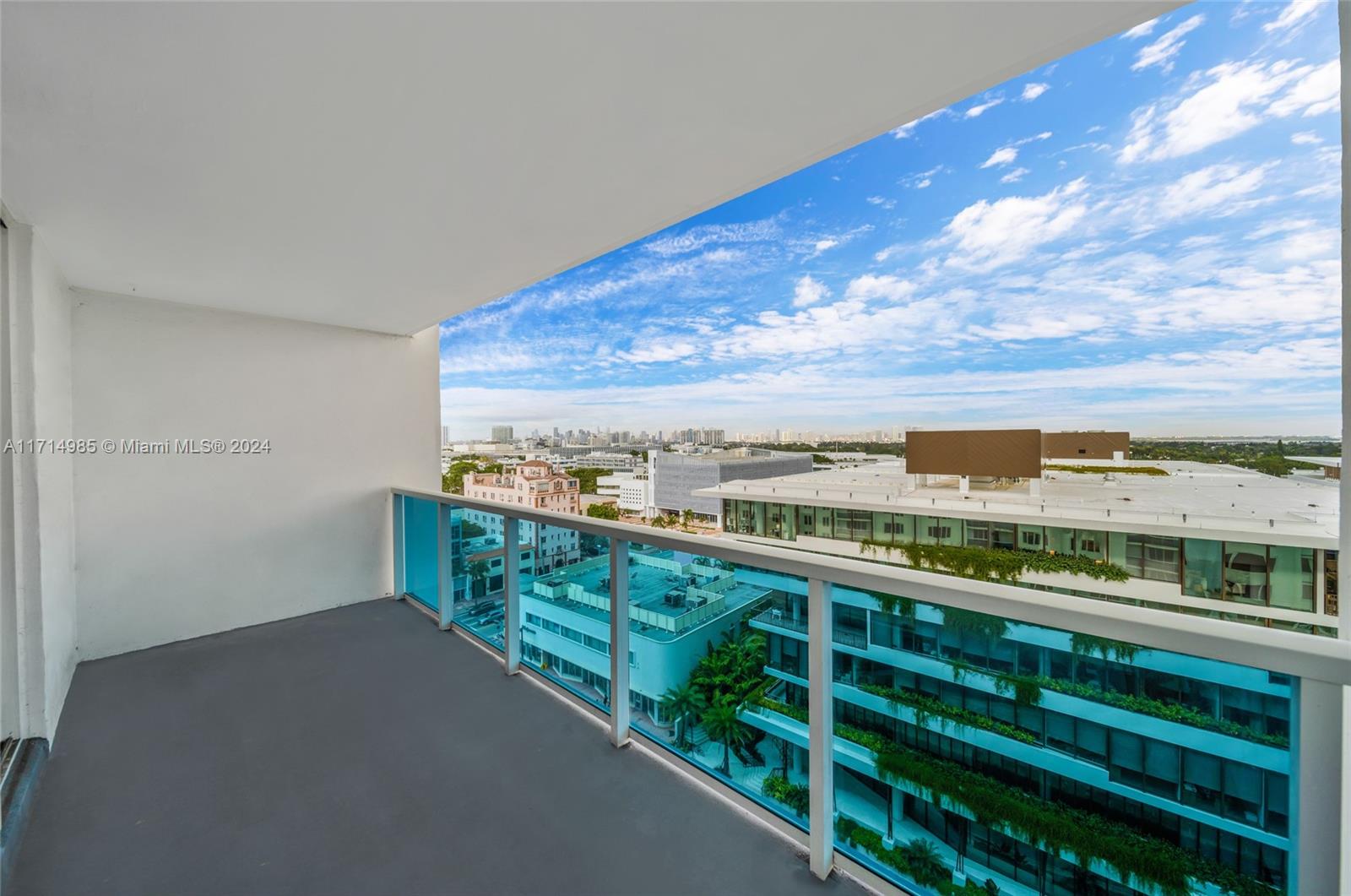 A balcony with a gray floor and glass railing overlooks a city skyline — 2301 Collins Ave # 1030, Miami Beach FL 33139, MIAMI BEACH, FL