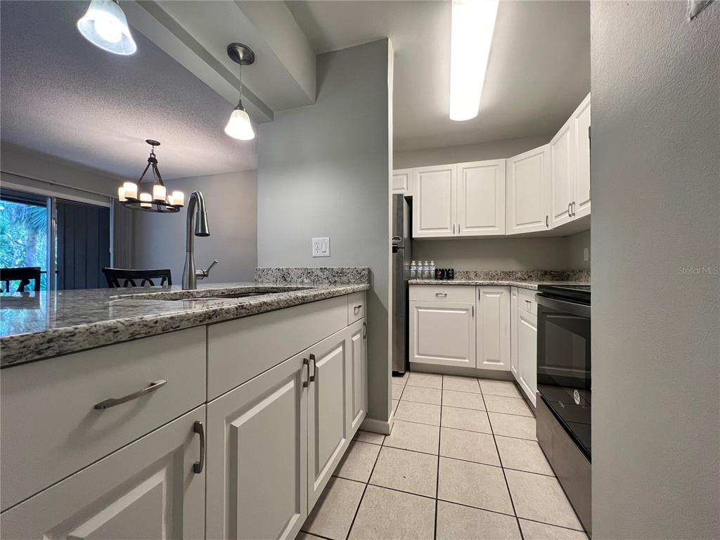 A kitchen features white cabinets, granite countertops, tile flooring, and a breakfast bar — 100 SWEETGUM WOODS COURT UNIT 3D, DELTONA, FL