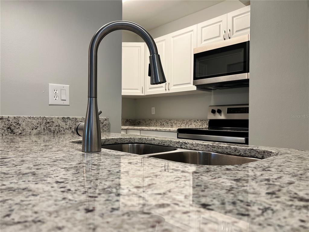 A kitchen features a stainless steel faucet, a double-basin sink, granite countertops, and white cabinets — 100 SWEETGUM WOODS COURT UNIT 3D, DELTONA, FL