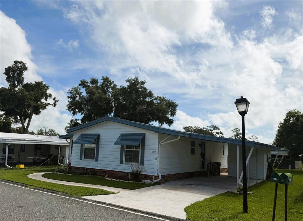 A single-story mobile home with white siding, blue trim, and an attached carport — 139 ASPEN CIRCLE, LEESBURG, FL