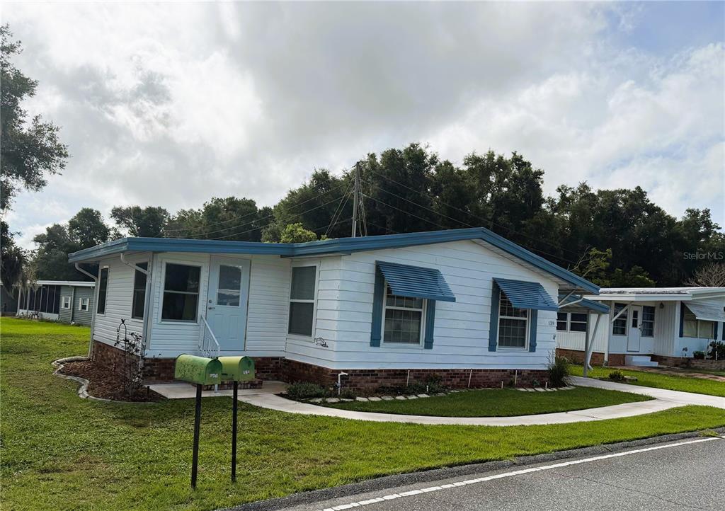 A white manufactured home with blue trim and awnings sits on a grassy lot — 139 ASPEN CIRCLE, LEESBURG, FL