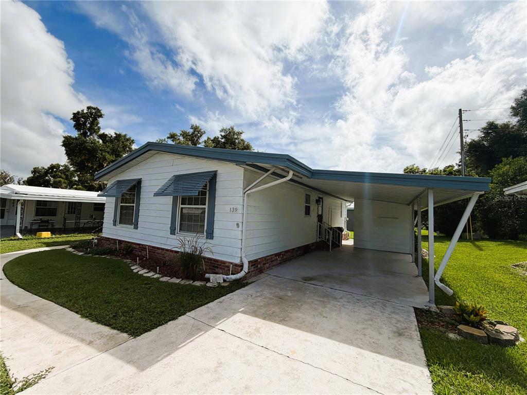 A single-story mobile home with white siding, a brick base, and an attached carport — 139 ASPEN CIRCLE, LEESBURG, FL