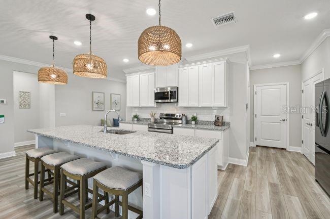 A kitchen features a granite-topped island with bar stools, white cabinetry, and three pendant lights — 3395 MONARCH WAY, GREEN COVE SPRINGS, FL