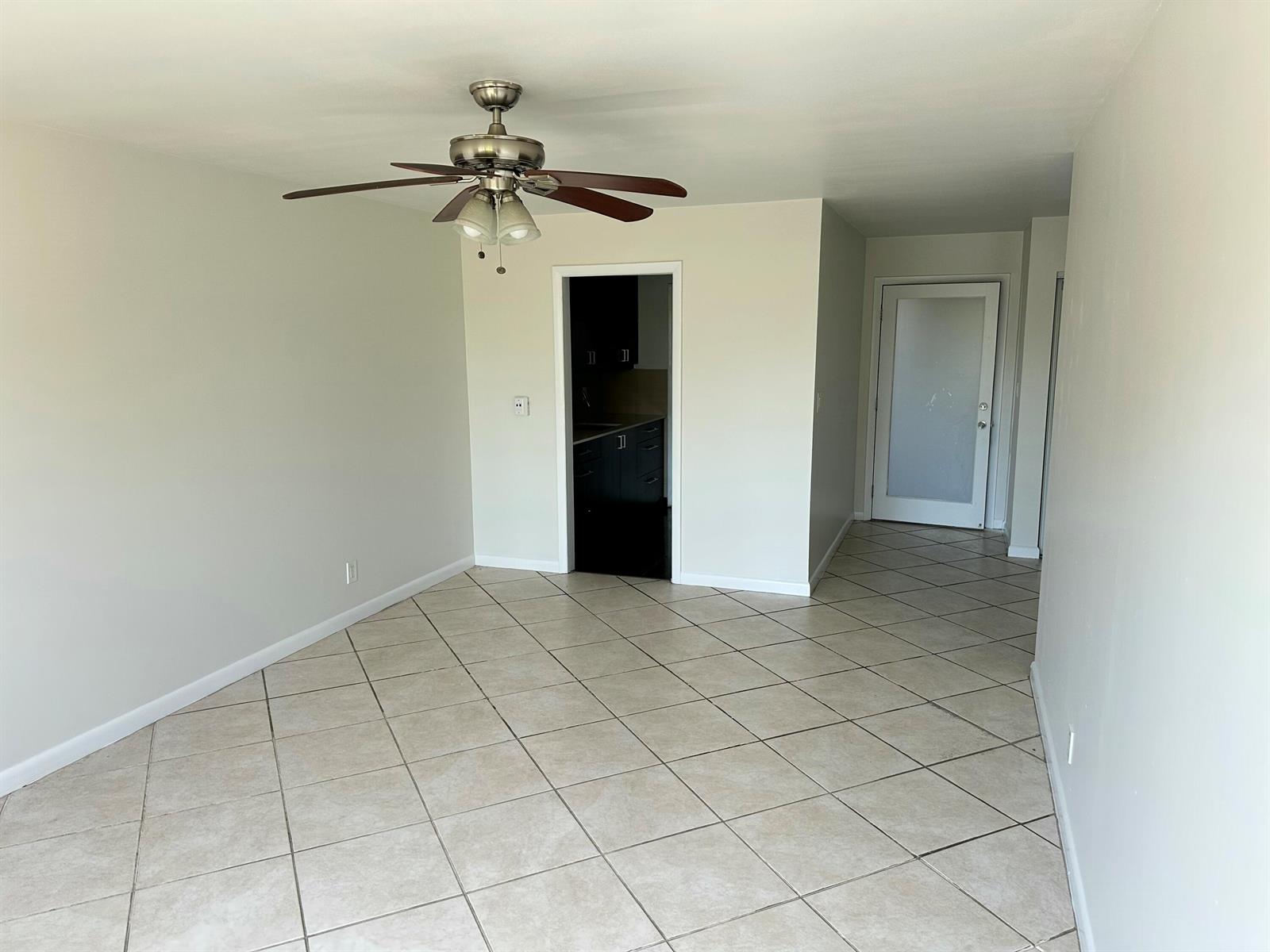 An empty room with beige tile flooring, a ceiling fan, and a doorway to a kitchen — 1480 E Sample Road # 207, Pompano Beach FL 33064, POMPANO BEACH, FL
