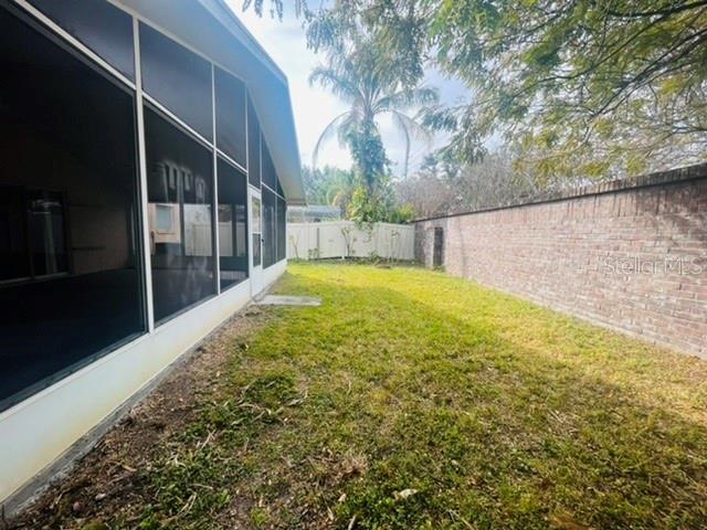 A narrow backyard features a screened-in porch, a brick wall, and a palm tree — 2861 FALLING TREE CIRCLE, ORLANDO, FL