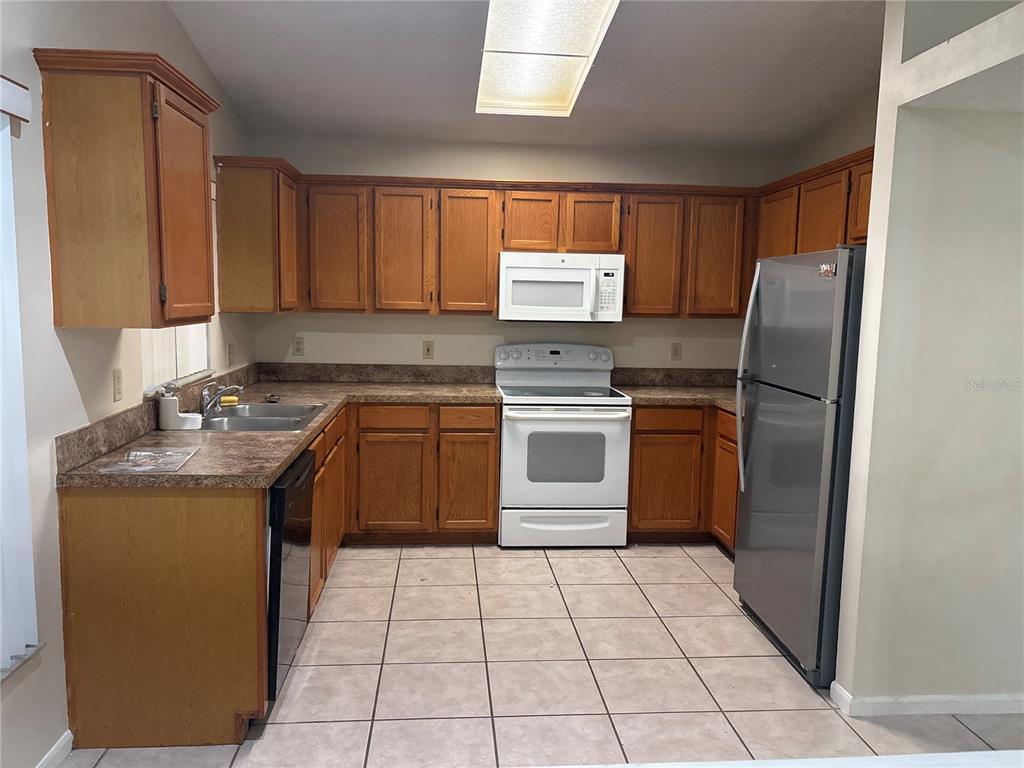 A kitchen features wood cabinets, laminate countertops, white appliances, and a stainless steel refrigerator — 2861 FALLING TREE CIRCLE, ORLANDO, FL