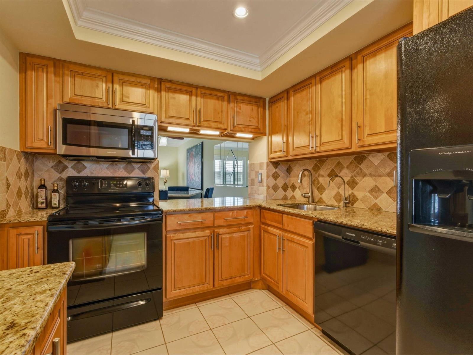 A kitchen with light wood cabinets, granite countertops, tile backsplash, and black appliances — 9810 Marina Boulevard # 1136, Boca Raton FL 33428, BOCA RATON, FL