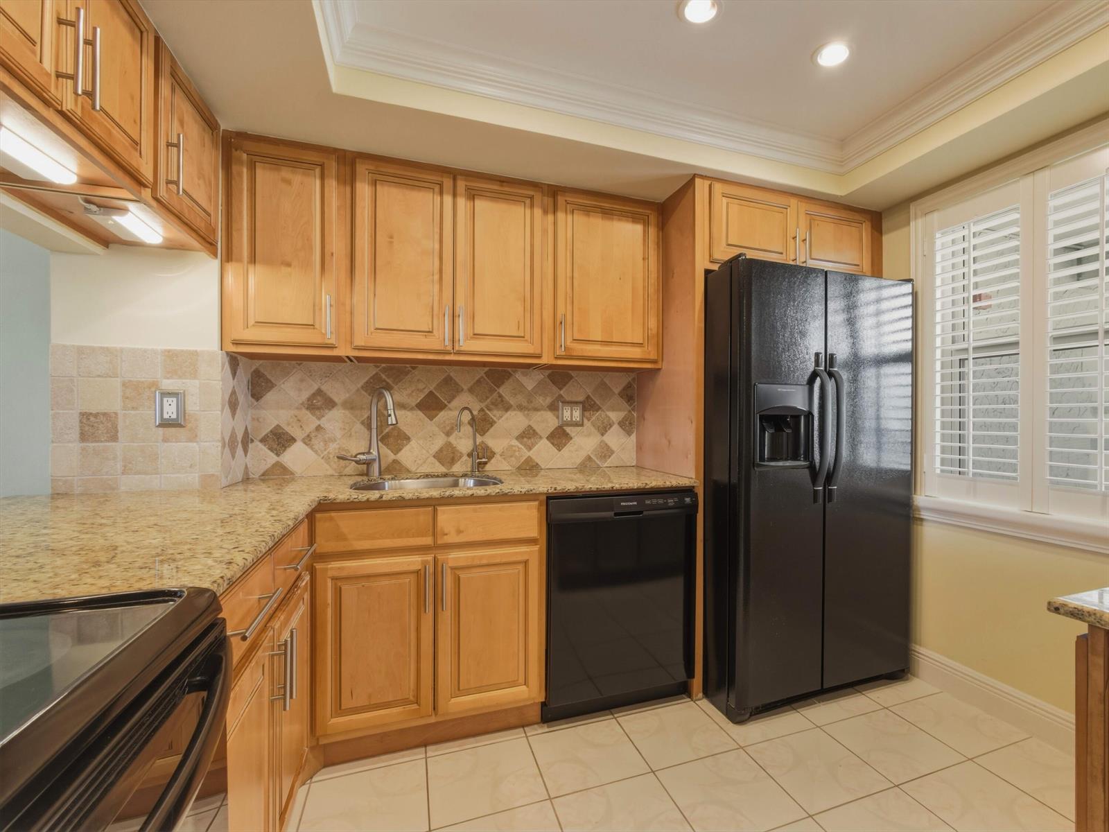 A kitchen features light wood cabinets, granite countertops, a black refrigerator, and a tiled backsplash — 9810 Marina Boulevard # 1136, Boca Raton FL 33428, BOCA RATON, FL