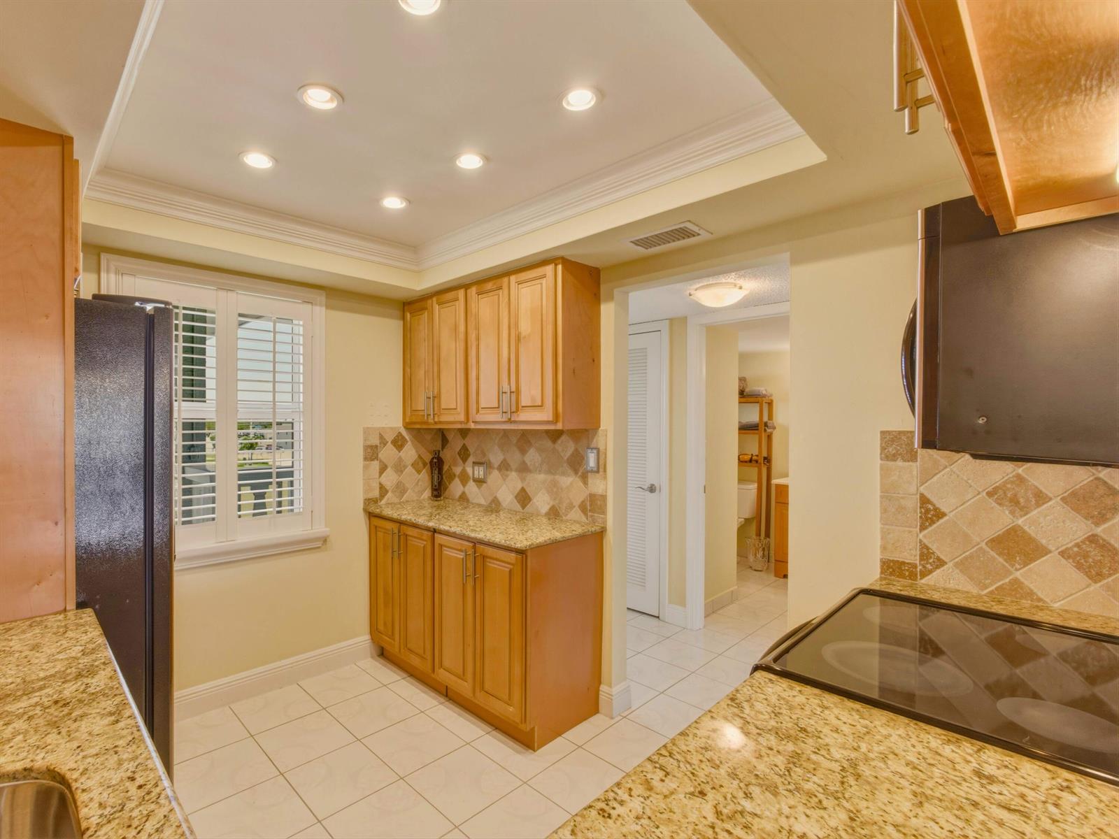 A kitchen features light wood cabinets, granite countertops, tile backsplash, and a tiled floor — 9810 Marina Boulevard # 1136, Boca Raton FL 33428, BOCA RATON, FL