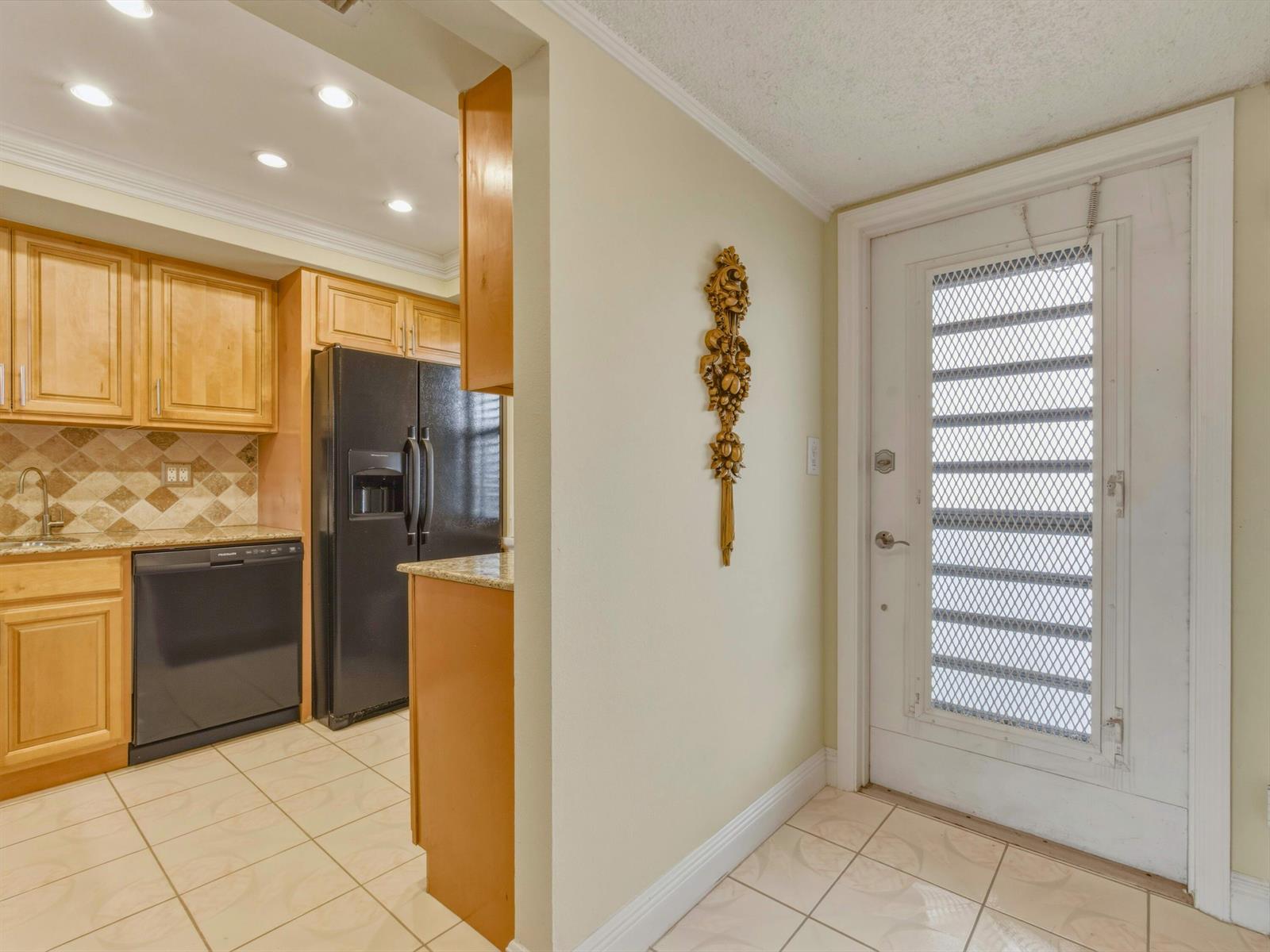 A kitchen with light wood cabinets and black appliances sits beside a white entry door — 9810 Marina Boulevard # 1136, Boca Raton FL 33428, BOCA RATON, FL