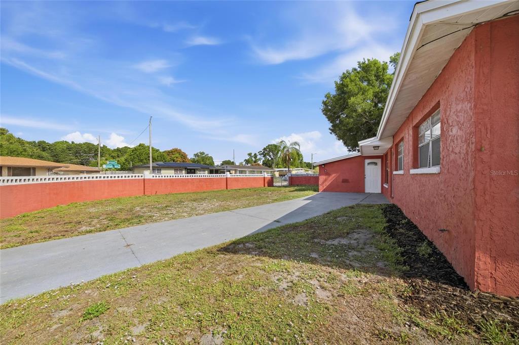 A red stucco house exterior features a concrete driveway leading to a white side door — 7102 DELLWOOD DRIVE, TAMPA, FL