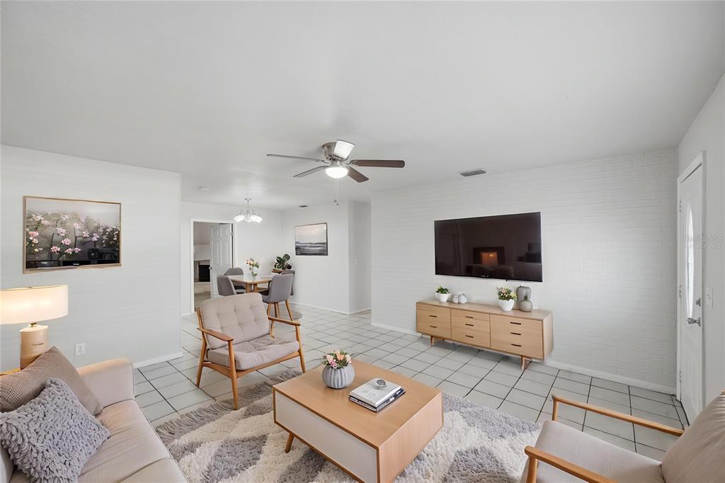 A living room features white brick walls, tile flooring, a ceiling fan, and modern furniture — 7102 DELLWOOD DRIVE, TAMPA, FL