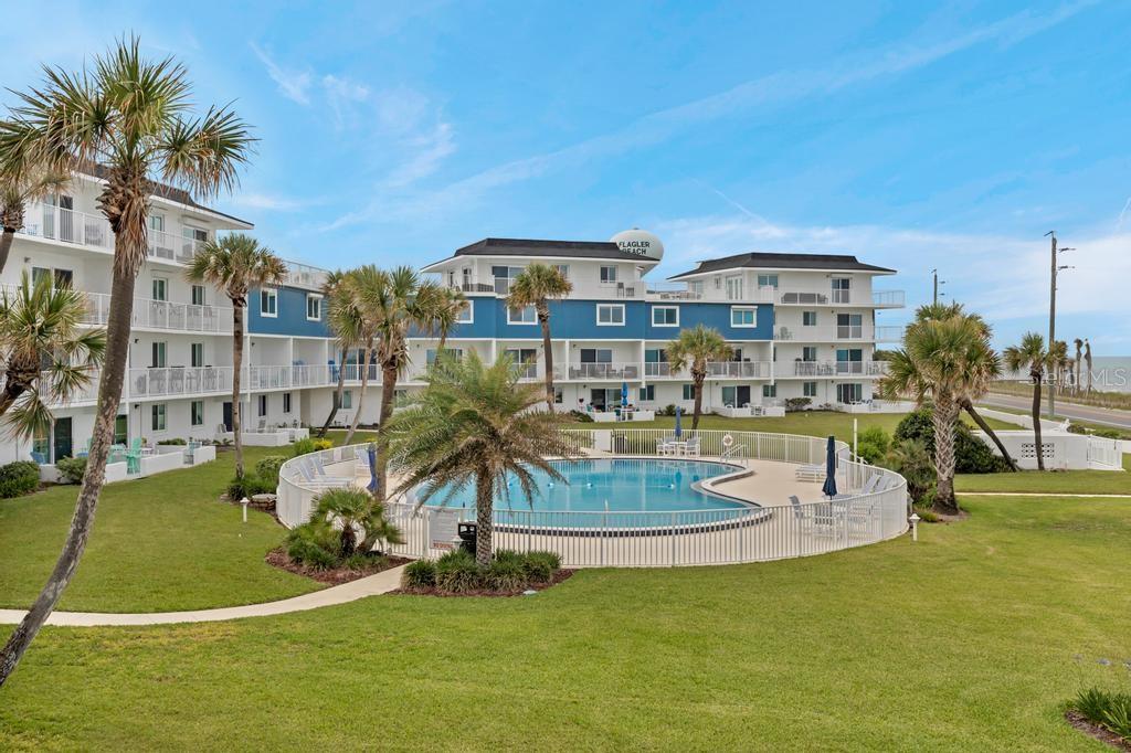 An exterior view of a multi-story apartment building with a swimming pool and palm trees — 3510 S OCEAN SHORE BOULEVARD UNIT 203, FLAGLER BEACH, FL
