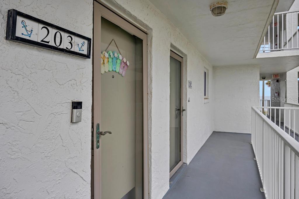 An exterior hallway shows the entrance to unit 203 with a beach-themed door sign — 3510 S OCEAN SHORE BOULEVARD UNIT 203, FLAGLER BEACH, FL