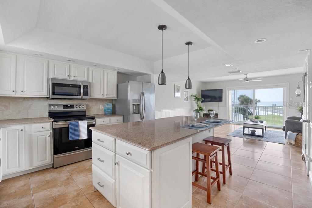 A kitchen with white cabinets, granite countertops, and an island overlooks a living area — 3510 S OCEAN SHORE BOULEVARD UNIT 203, FLAGLER BEACH, FL