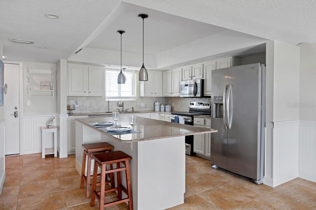 A kitchen features white cabinetry, granite countertops, a center island with stools, and stainless appliances — 3510 S OCEAN SHORE BOULEVARD UNIT 203, FLAGLER BEACH, FL
