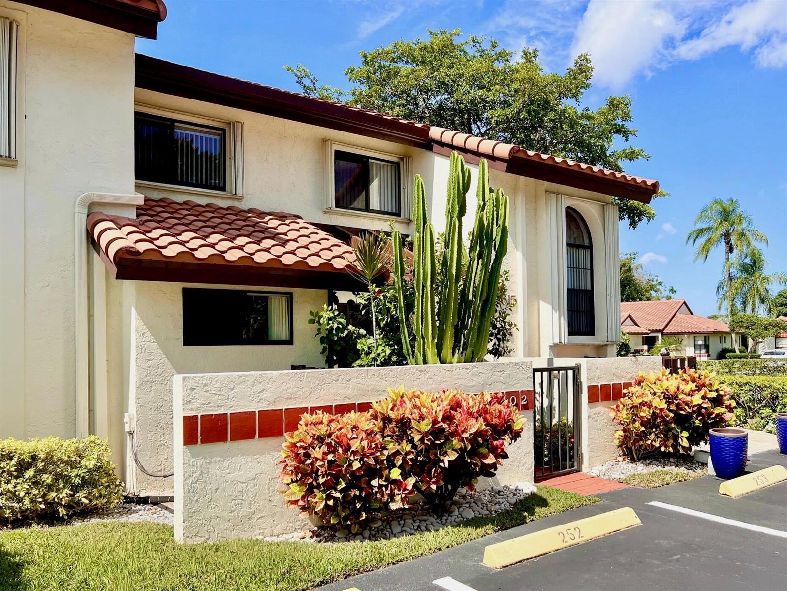 A two-story stucco townhouse features a tiled roof, a small front patio, and landscaping — 10615 Ocean Palm Way # 102, Boynton Beach FL 33437, BOYNTON BEACH, FL