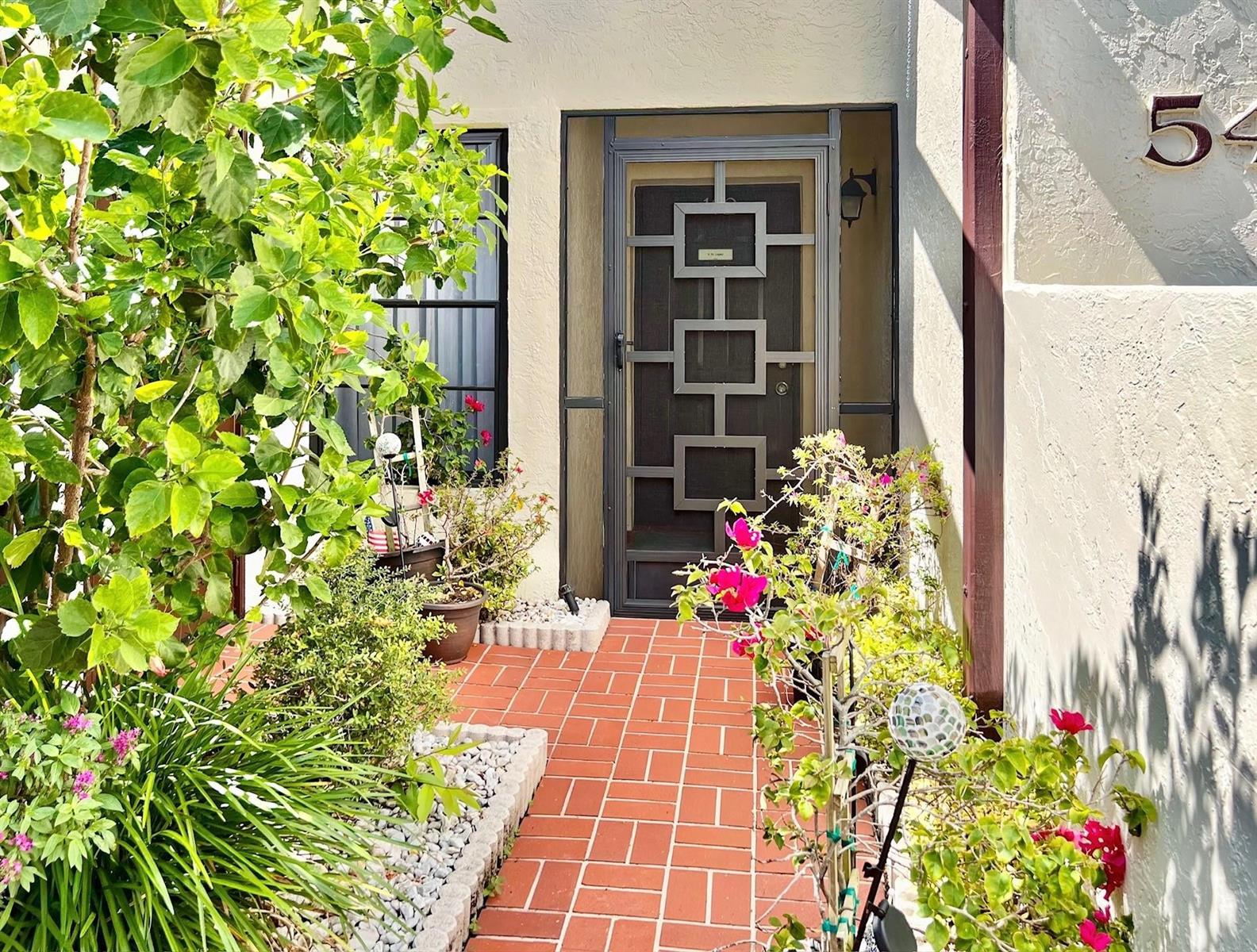 A brick walkway leads to a front door with a geometric metal security screen — 10615 Ocean Palm Way # 102, Boynton Beach FL 33437, BOYNTON BEACH, FL