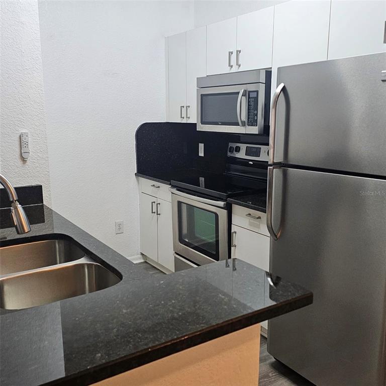 A kitchen features white cabinets, stainless steel appliances, and black countertops — 3599 CONROY ROAD UNIT 934, ORLANDO, FL