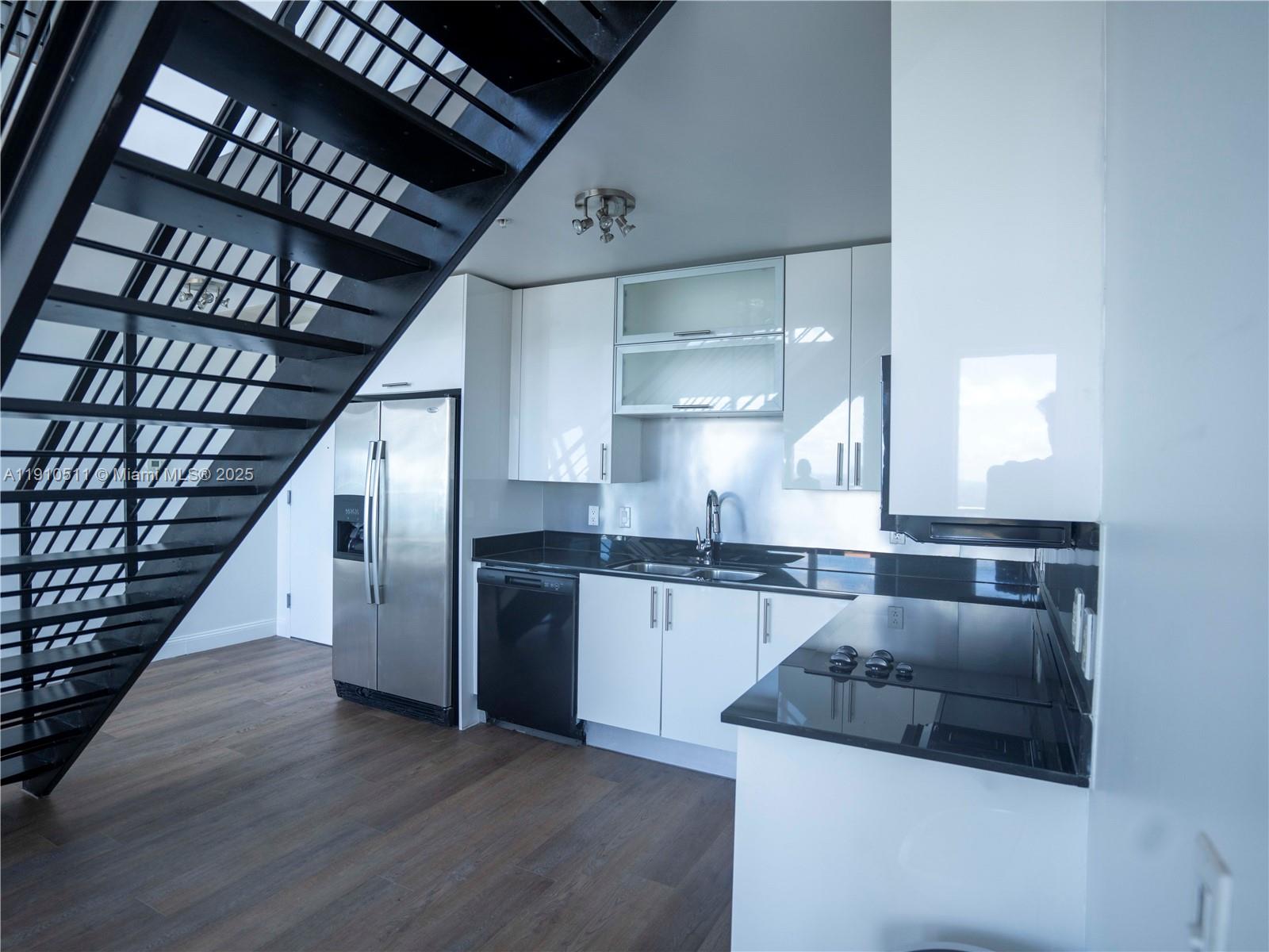 A modern kitchen features white cabinets, black countertops, stainless steel appliances, and a black staircase — 60 SW 13th St # 4805, Miami FL 33130, MIAMI, FL