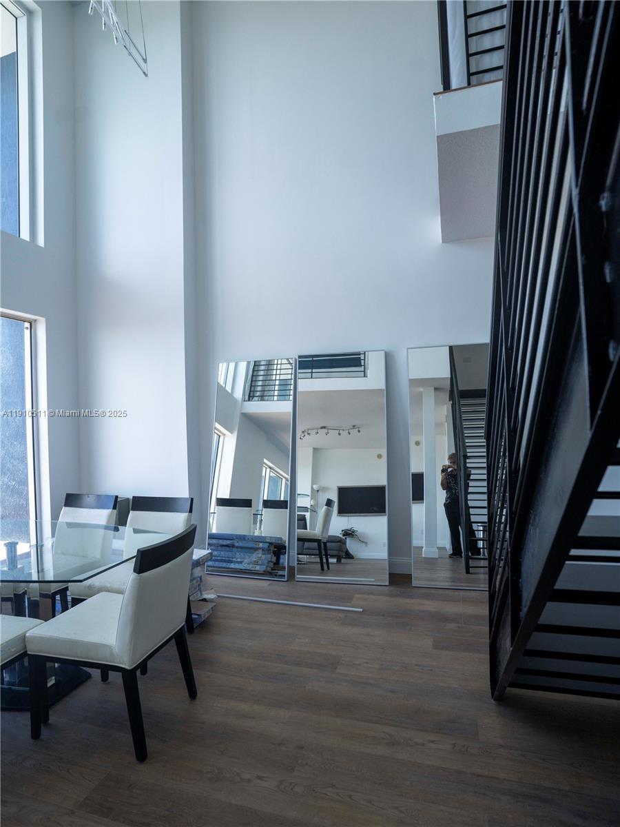 A dining area features a glass table, white chairs, tall mirrors, and a black staircase — 60 SW 13th St # 4805, Miami FL 33130, MIAMI, FL