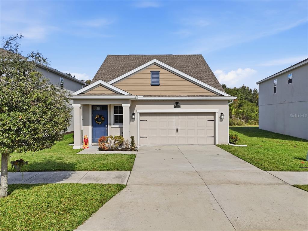A single-story suburban house with a tan exterior, blue front door, and two-car garage — 4303 SEVEN CANYONS DRIVE, KISSIMMEE, FL