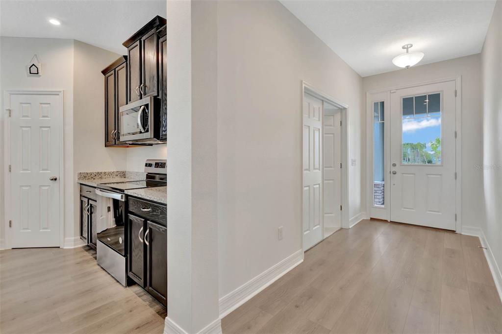 A kitchen with dark cabinets and stainless appliances sits adjacent to an entryway with wood flooring — 3112 AMBERSWEET PLACE, CLERMONT, FL