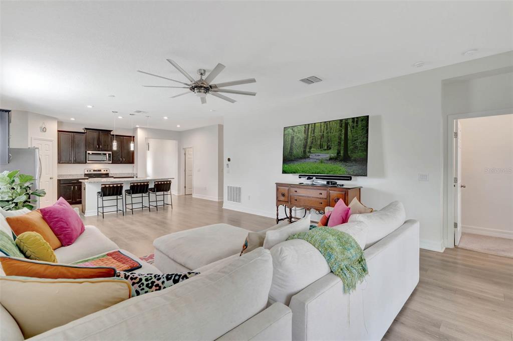 An open-concept living room features a white sectional sofa, a television, and a kitchen island — 3112 AMBERSWEET PLACE, CLERMONT, FL