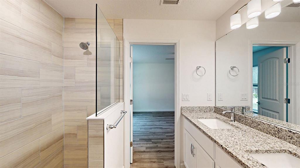 A bathroom features a tiled walk-in shower, a granite-topped vanity, and a doorway to a bedroom — 3438 ALWOOD STREET, NORTH PORT, FL