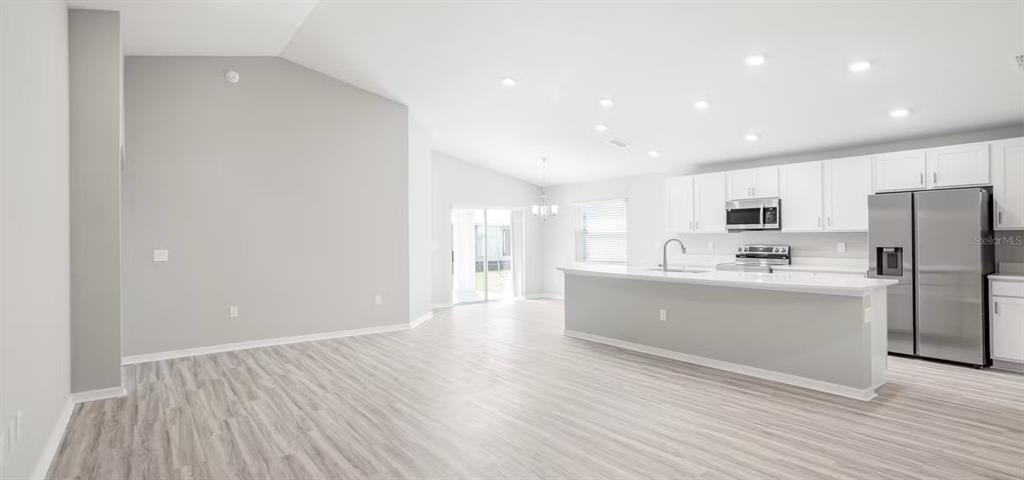 An open-concept kitchen and living area features white cabinetry, stainless steel appliances, and light flooring — 11559 SE 76TH COURT, BELLEVIEW, FL
