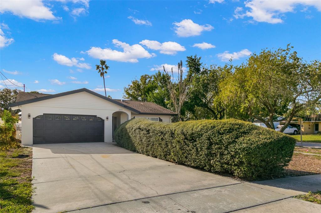 A single-story house features a dark garage door, a concrete driveway, and a large hedge — 5931 DENVER STREET NE, ST PETERSBURG, FL