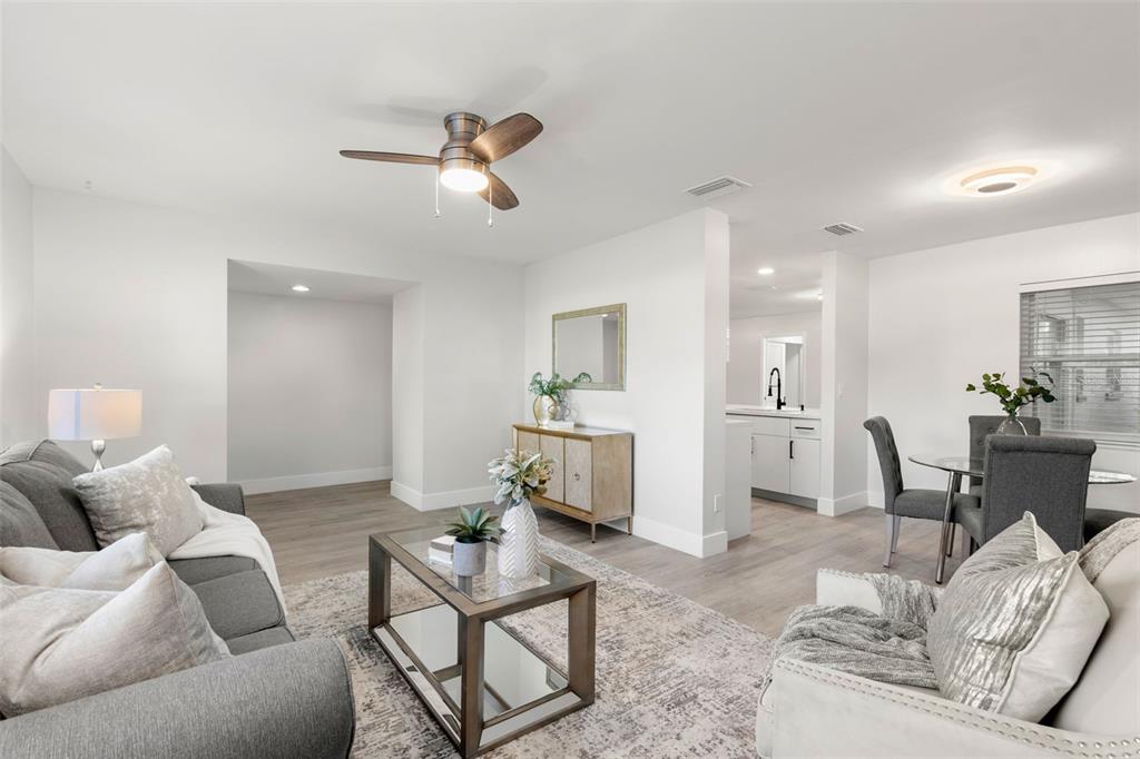 A living room with gray furniture, a glass coffee table, and light wood-look flooring — 5931 DENVER STREET NE, ST PETERSBURG, FL