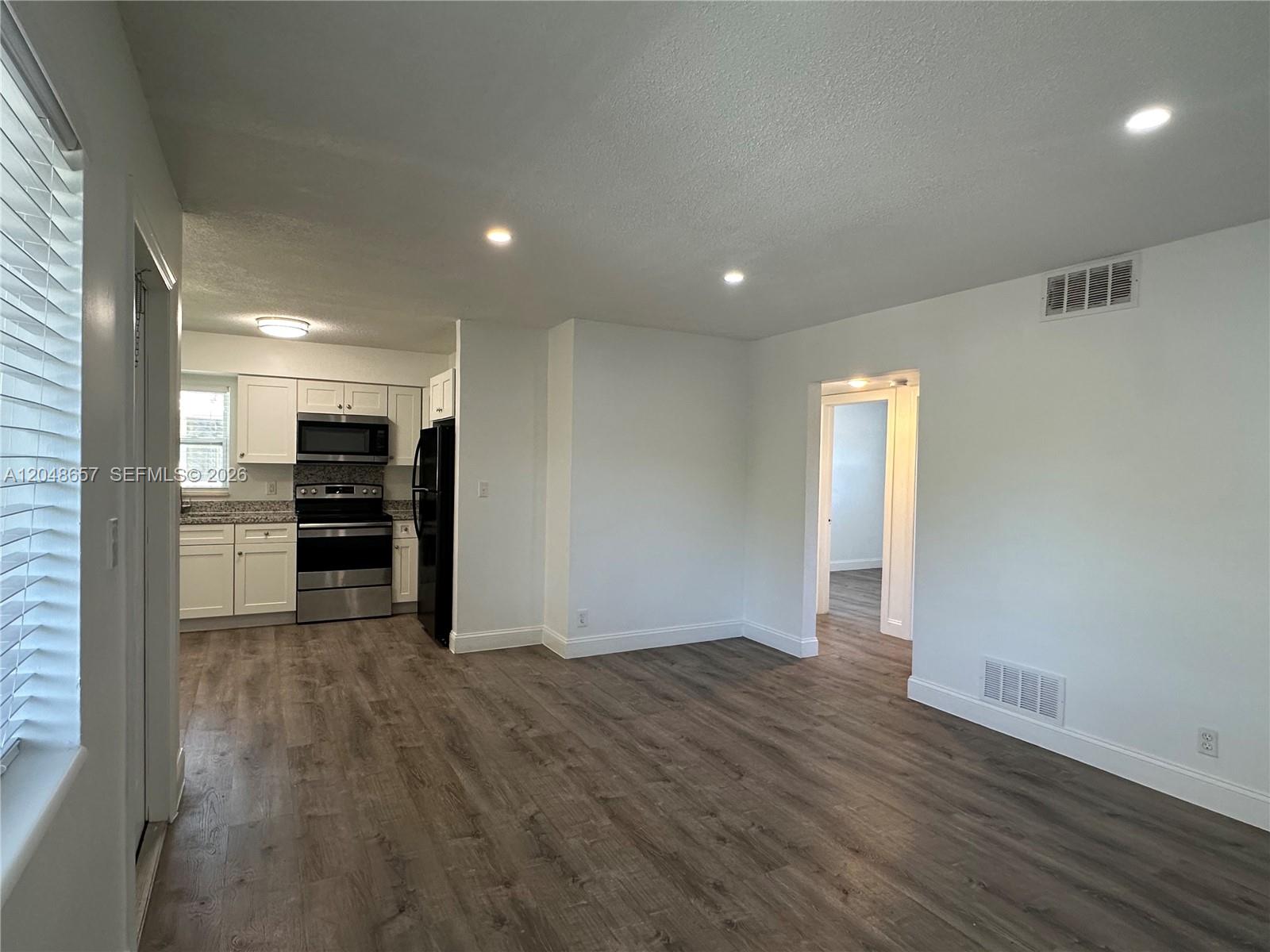 A kitchen with white cabinets and stainless steel appliances opens into a living area — 2401 NW 9th Ave # 3, Wilton Manors FL 33311, WILTON MANORS, FL