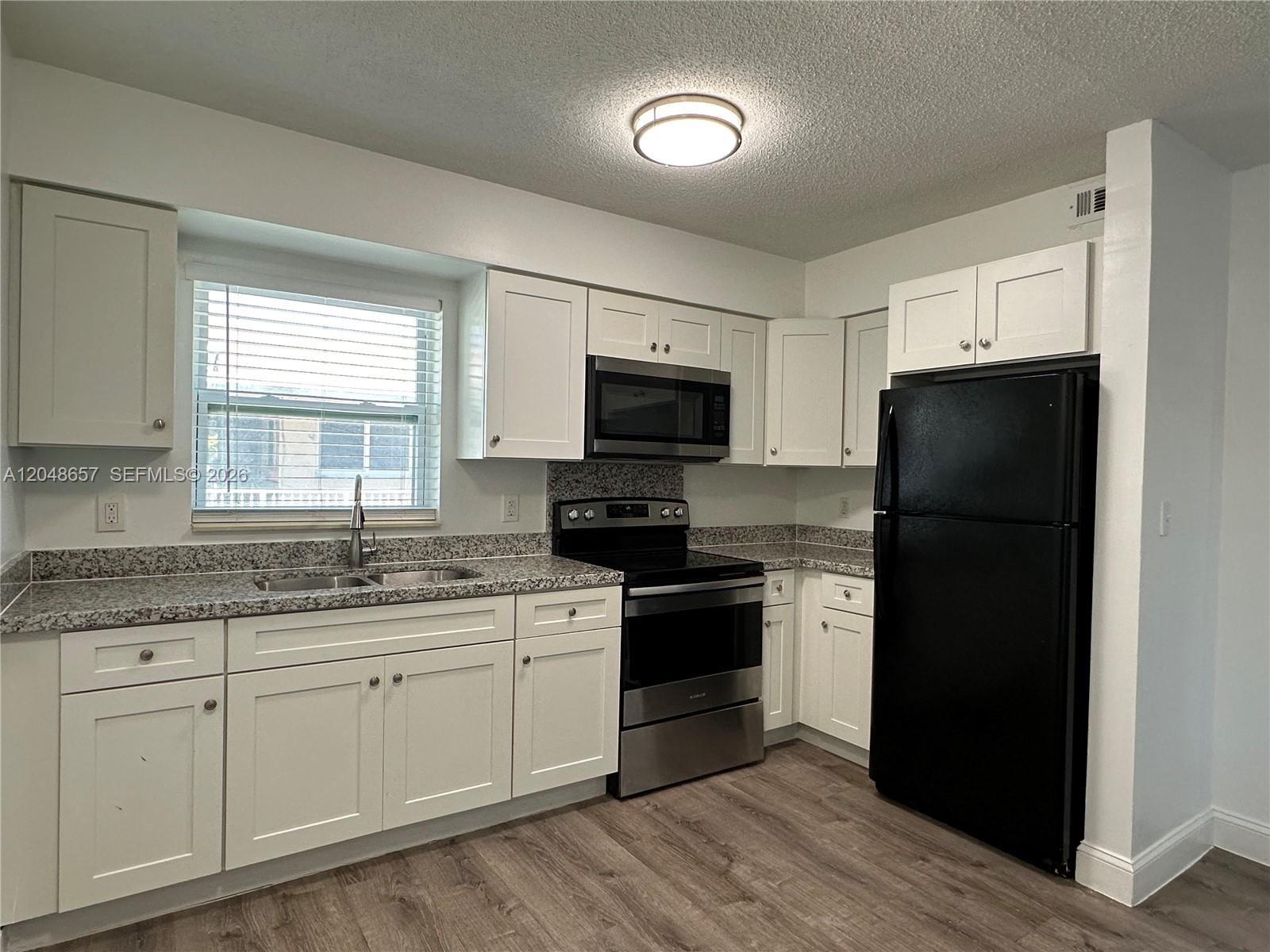 A kitchen features white cabinets, granite countertops, stainless steel appliances, and a black refrigerator — 2401 NW 9th Ave # 3, Wilton Manors FL 33311, WILTON MANORS, FL