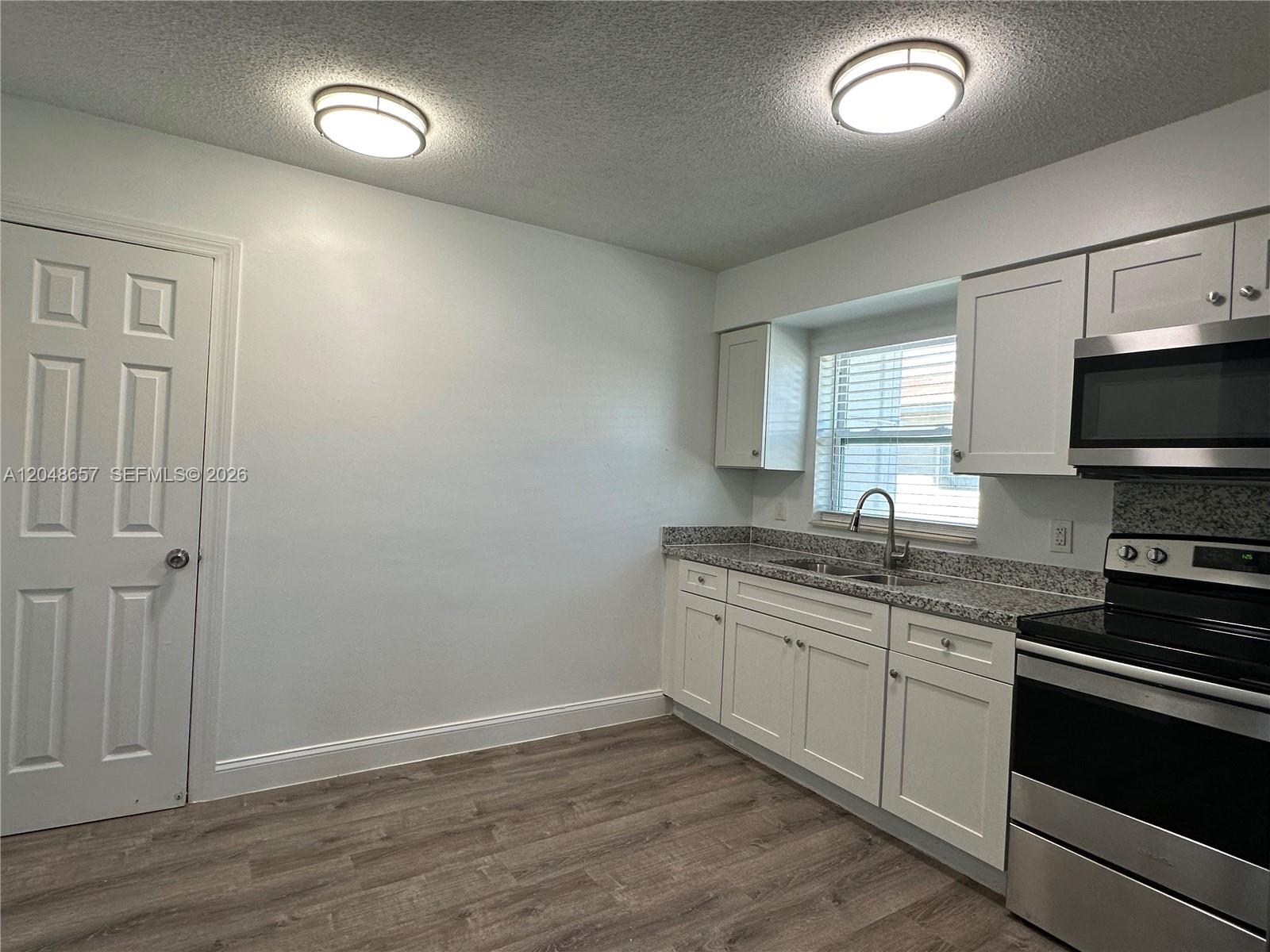 A kitchen features white cabinets, granite countertops, stainless steel appliances, and wood-look flooring — 2401 NW 9th Ave # 3, Wilton Manors FL 33311, WILTON MANORS, FL