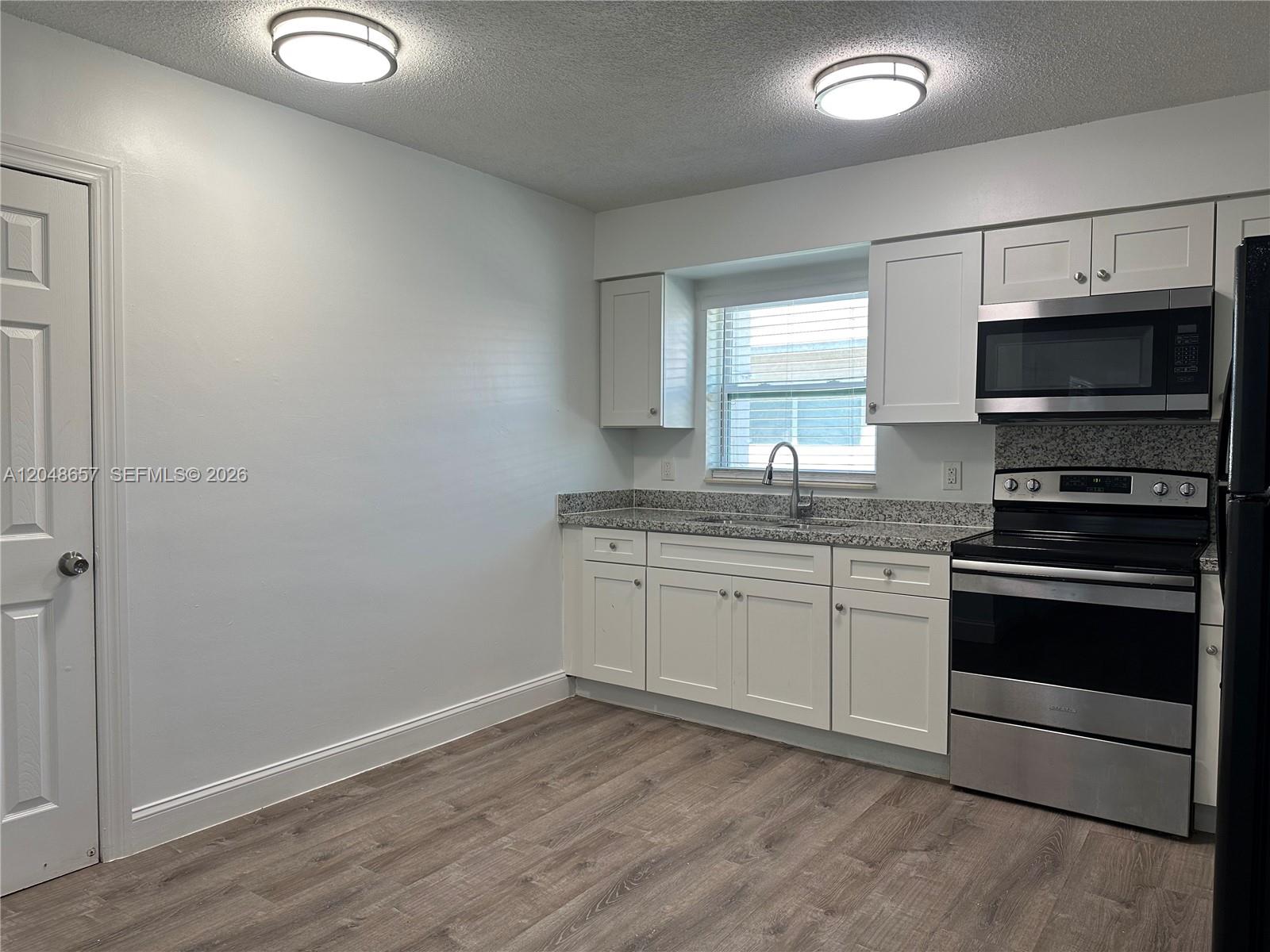 A kitchen features white cabinets, granite countertops, stainless steel appliances, and wood-look flooring — 2401 NW 9th Ave # 3, Wilton Manors FL 33311, WILTON MANORS, FL