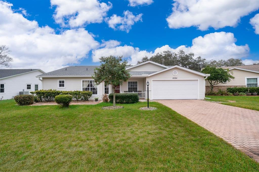 A single-story house with light siding, a two-car garage, and a brick paver driveway — 25741 BELLE HELENE, LEESBURG, FL