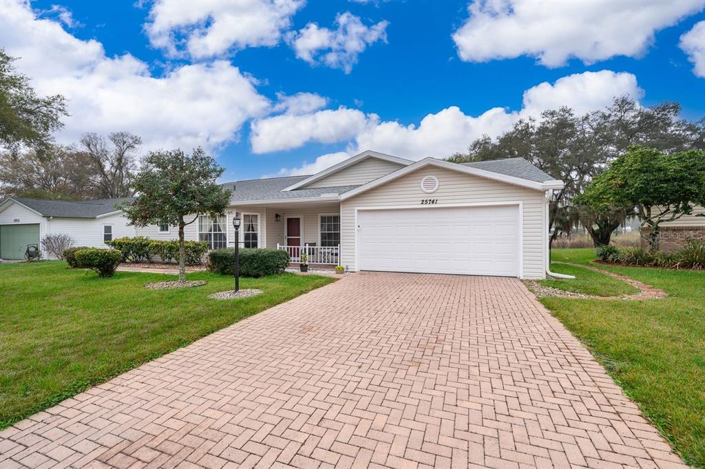 A single-story house with light siding, a two-car garage, and a brick-paved driveway — 25741 BELLE HELENE, LEESBURG, FL