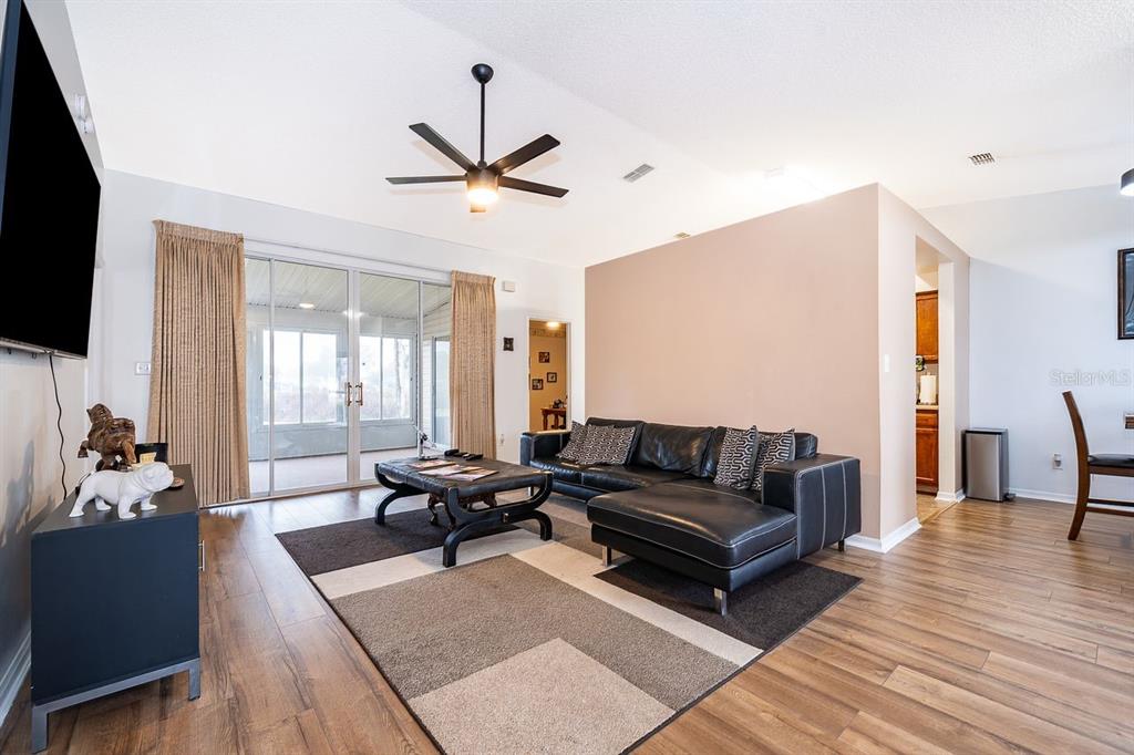 A living room features a black sectional sofa, wood-look flooring, and a sliding glass door — 25741 BELLE HELENE, LEESBURG, FL