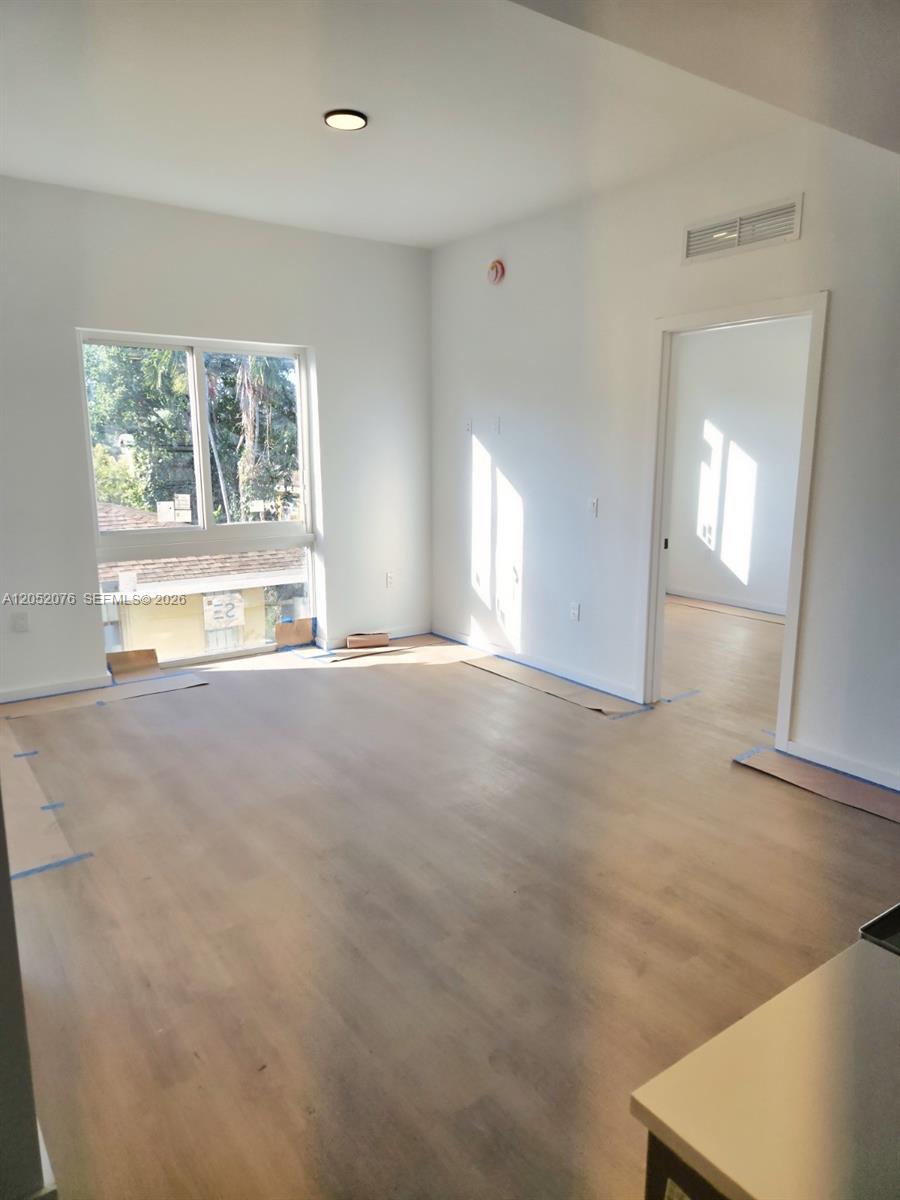An empty room with light wood-look flooring, white walls, and a window overlooking trees — 8106 NE 1st Ave # 8, Miami FL 33138, MIAMI, FL