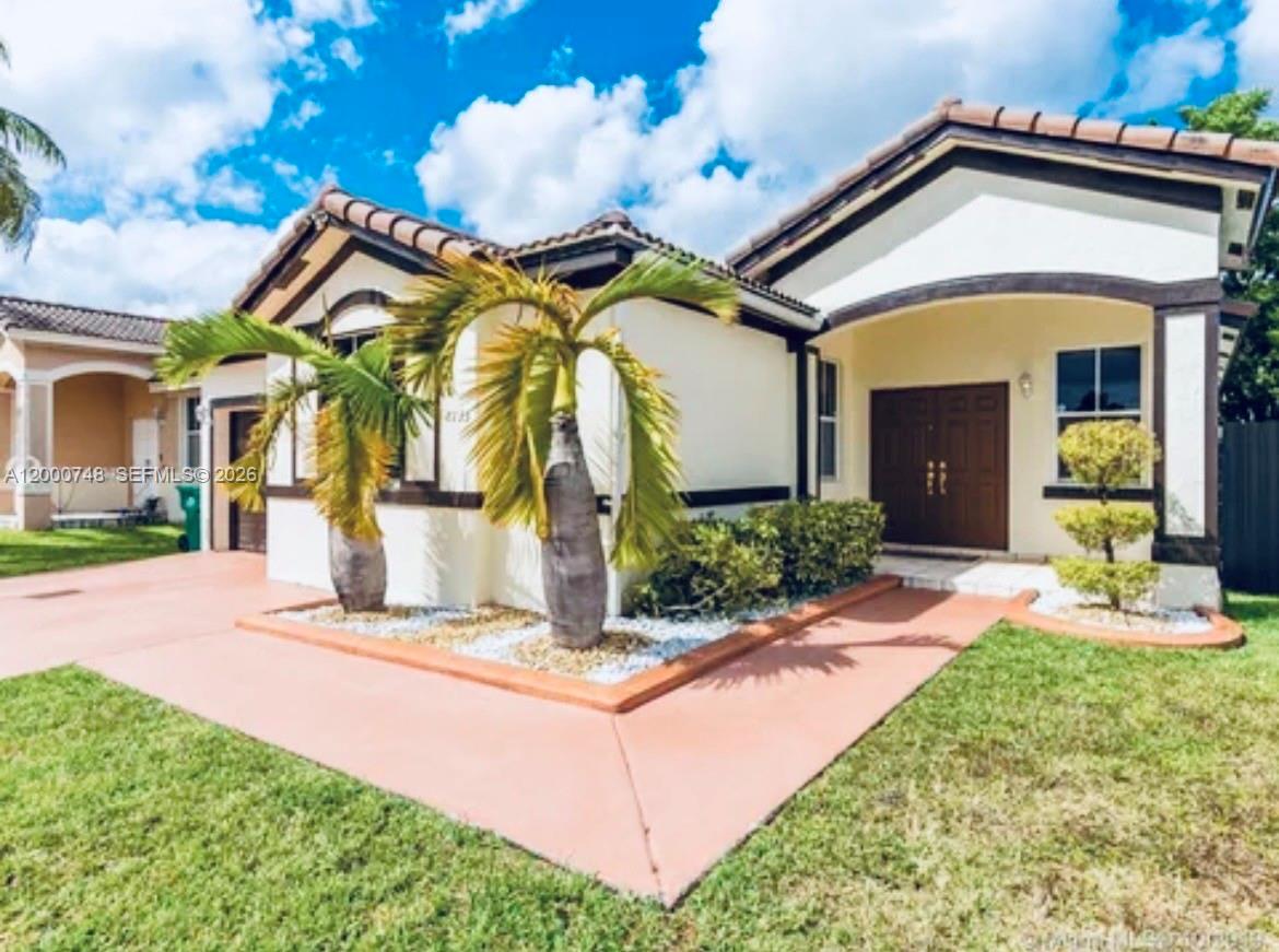 A single-story house with a tan stucco exterior, dark trim, palm trees, and a front walkway — 8135 NW 198th Ter, Hialeah FL 33015, HIALEAH, FL