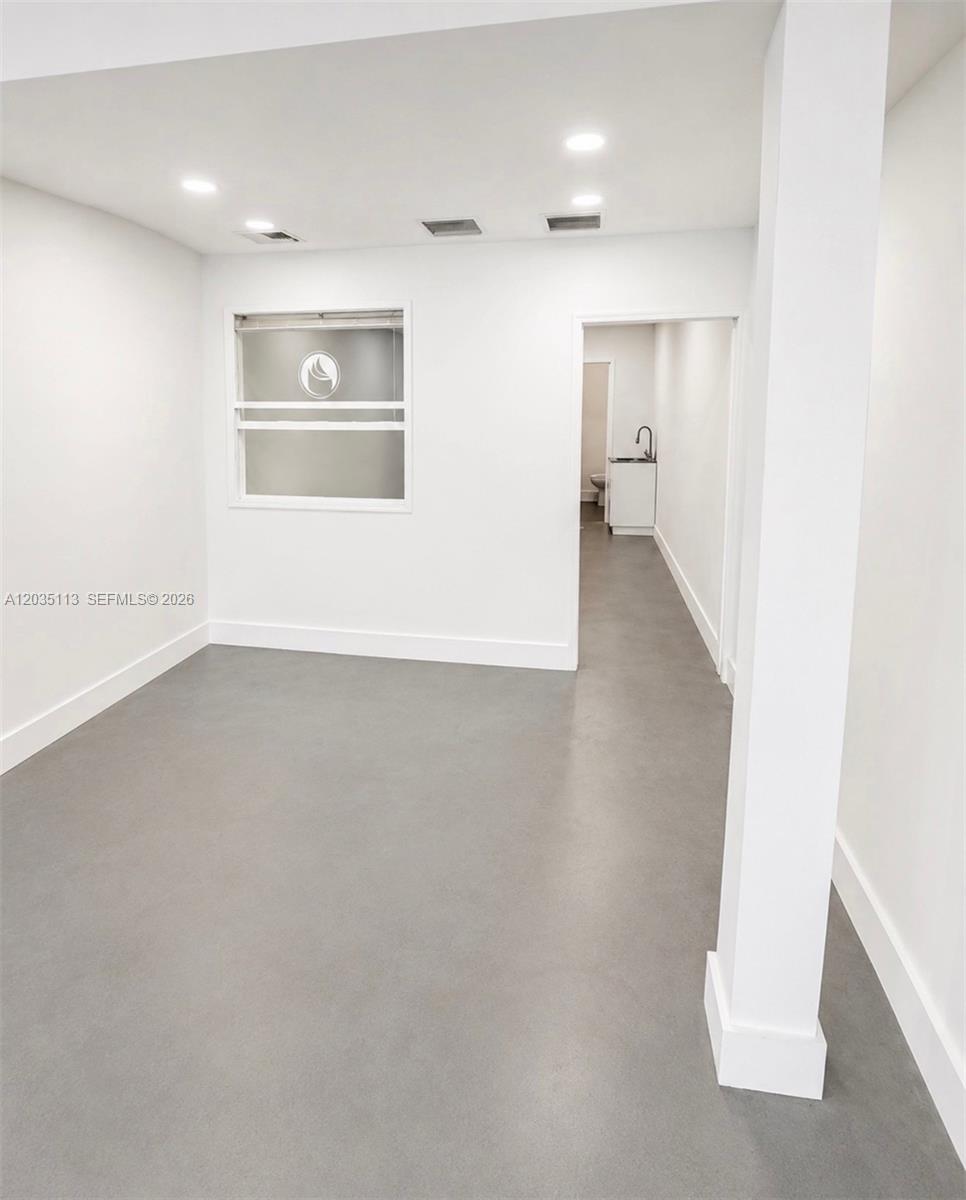 A minimalist room with gray concrete flooring, white walls, recessed lighting, and an attached bathroom — 29 S J St, FL 33460, FL