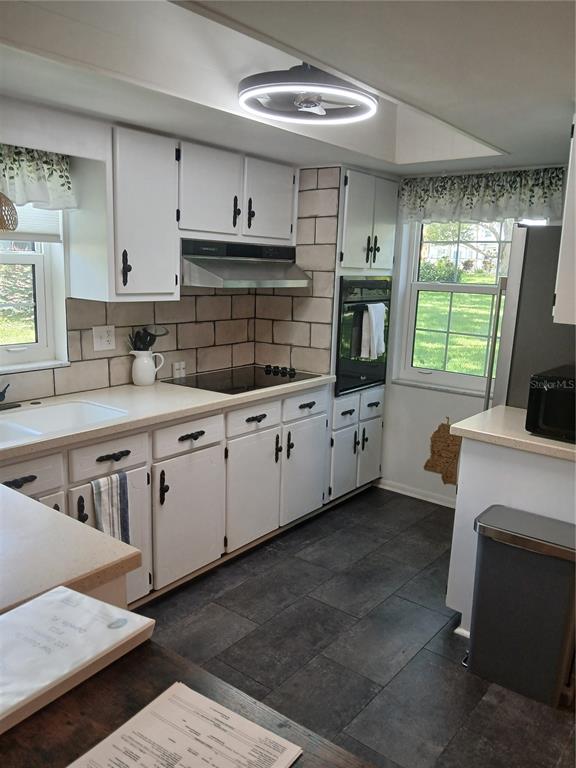 A kitchen features white cabinets, a tiled backsplash, dark tile flooring, and a ceiling fan — 200 GLENNES LANE UNIT 103, DUNEDIN, FL