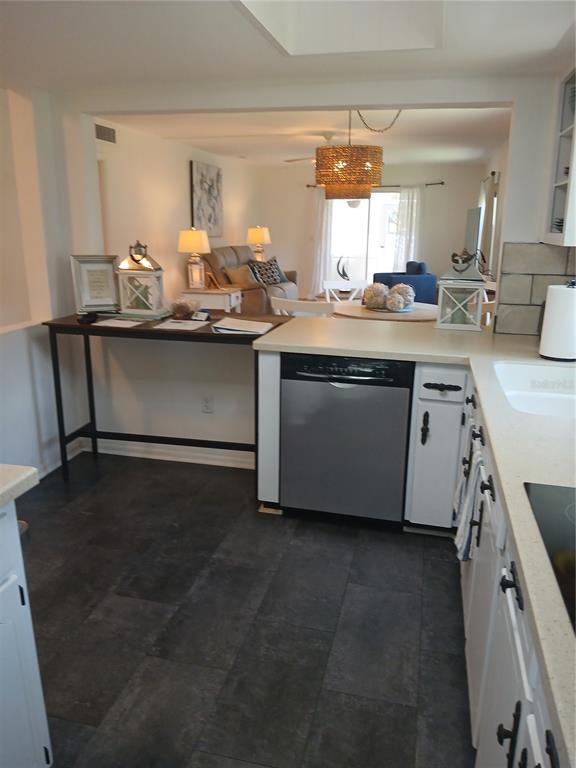 A kitchen with white cabinets and a dishwasher opens into a living area with tile flooring — 200 GLENNES LANE UNIT 103, DUNEDIN, FL