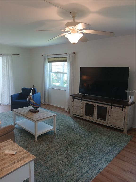 A living room features a ceiling fan, a large television, a coffee table, and rug — 200 GLENNES LANE UNIT 103, DUNEDIN, FL
