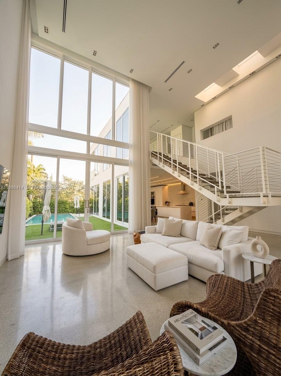 A bright living room features double-height windows, a white sofa, and a staircase overlooking a pool — 949 Tyler St, Hollywood FL 33019, HOLLYWOOD, FL