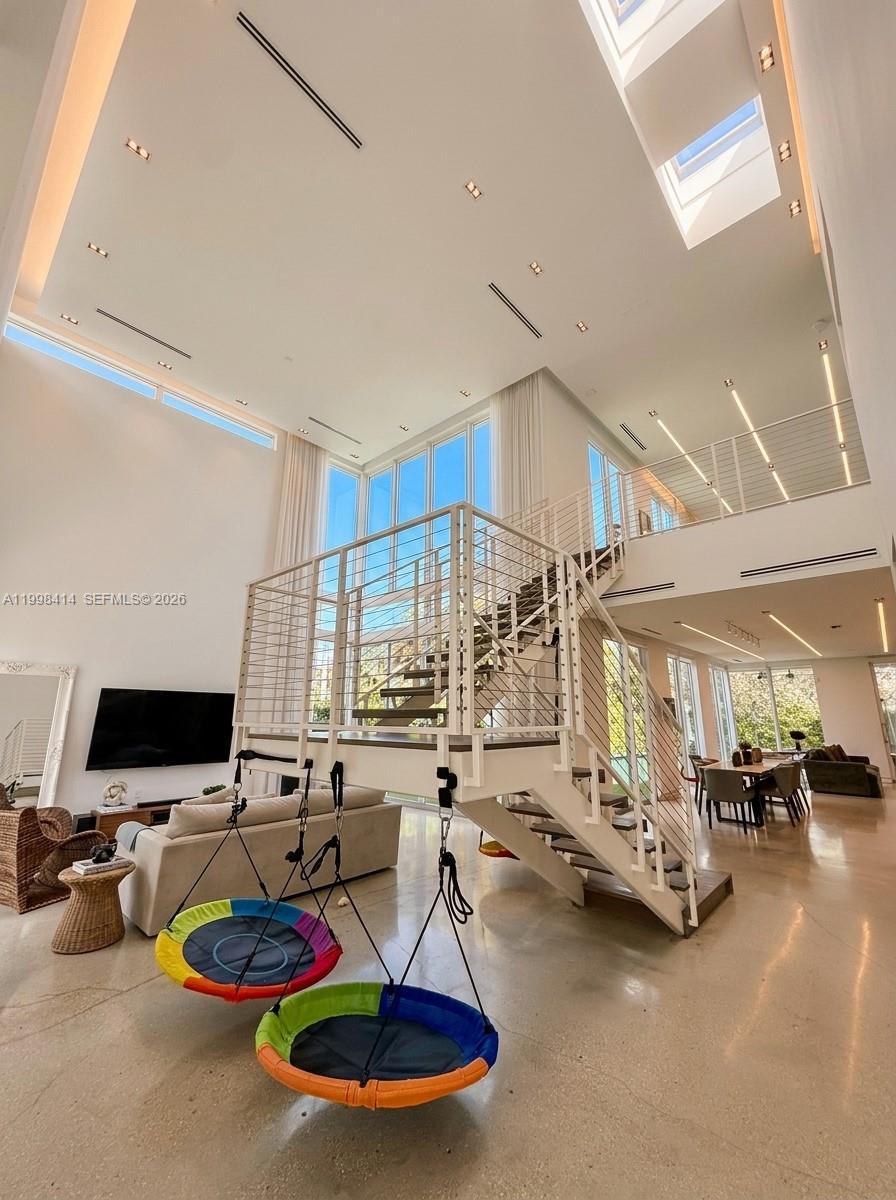 A modern, high-ceilinged living room features a central white staircase with two hanging saucer swings — 949 Tyler St, Hollywood FL 33019, HOLLYWOOD, FL