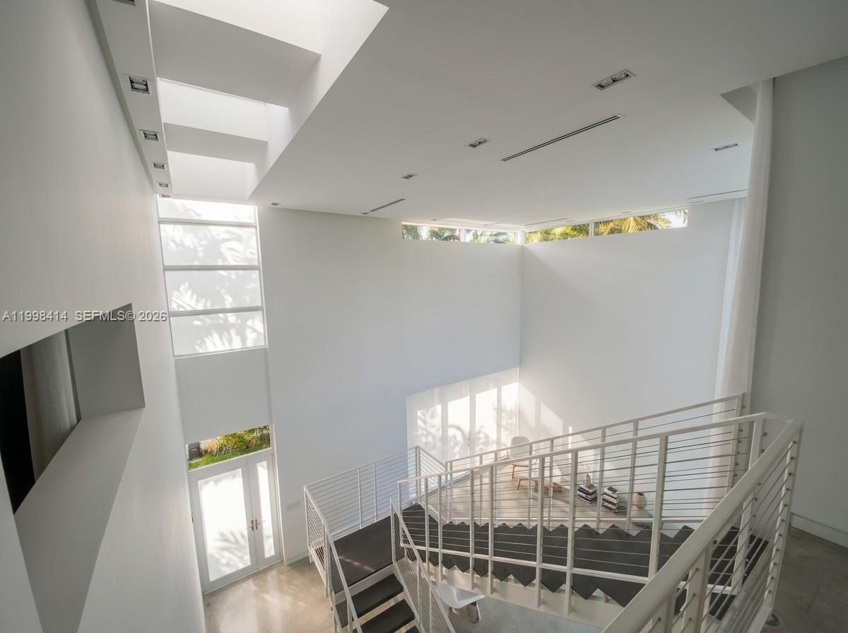 A high-ceilinged modern foyer features a white staircase with metal railings and large windows — 949 Tyler St, Hollywood FL 33019, HOLLYWOOD, FL