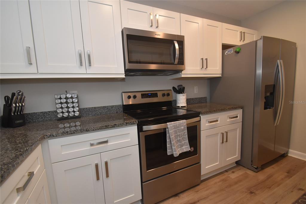 A kitchen features white cabinets, stainless steel appliances, and dark granite countertops — 1720 GLENHOUSE DRIVE UNIT GL427, SARASOTA, FL